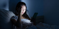 Jeune fille dans son lit souffrant d'insomnie lit un article de yoga sur son portable pour trouver le sommeil